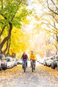 Two students ride down Greek Row in the 秋天, amid changing leaves.